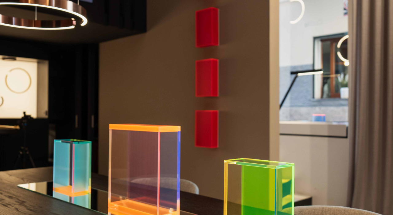 Vibrante decoración interior con bloques de acrílico en colores naranja, verde y azul colocados sobre una mesa, con elementos de fondo en tonos neutros y Espacios amplios.